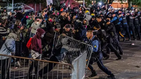 Getty Images Protesters and police clash outside Delaney Hall detention centre in Newark on 30 May. In the foreground, a masked protester pushes a metal barricade toward a police officer, who pushes back.