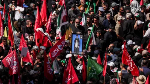 Iran supreme leader calls for revenge for father's killing Reuters Mourners gather for the burial of Iranian Supreme Leader Ali Khamenei in Mashhad. Many are carrying red flags with Arabic script and in the centre a man holds a picture of a sitting Khamenei, with his son Mojtaba standing above him.