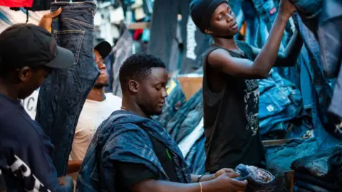 East Africa wants to curb imports of used clothes, but it's not easy AFP via Getty Images Three vendors handle jeans at a market stall