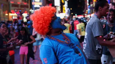 REUTERS/Shannon Stapleton Fan with a red fluffy wig and red and blue beads stands in profile in Times Square, tilting his head back and yelling  
