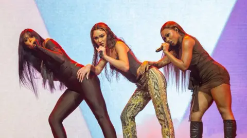 Girl group Flo on entering into their 'bombastic, confident, strong' era Getty Images Flo performing on stage. Jorja Douglas is to the left in a black skin tight catsuit. Stella Quaresma is on the middle in a brown top and animal print trousers. Renee Downer is on the right in a brown dress and black boots.