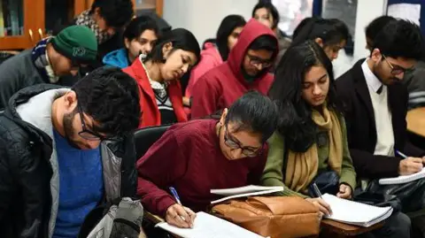 Currency crash and visa crackdowns force Indian students to rethink studying abroad Getty Images Students wearing woolens - jackets, scarves and sweaters - take notes in a class at the Ramjas College of Delhi University