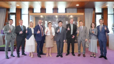 China bans four New Zealand MPs over Taiwan visit Lin Chia-lung/Facebook A row of men and women in formal attire flashing the thumbs-up sign to the camera.