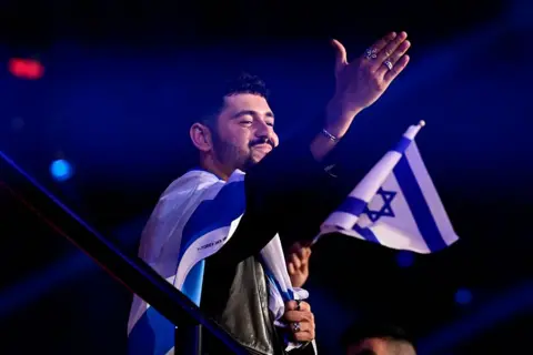 Getty Images Noam Bettan, carrying an Israeli flag, waves to the audience at Vienna's Wiener Stadthalle