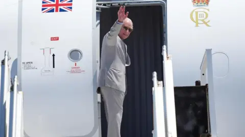 PA Media The King boards a plane with the Union Jack and turns to wave. He wears sunglasses.