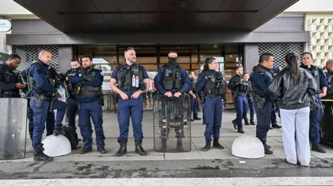 Getty Images Dozens of French police officers line up outside a store, wearing security vests and with one holding a riot shield.