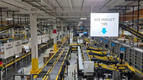 Inside Amazon's Darlington fulfilment centre with grey trays going along a yellow conveyor belt