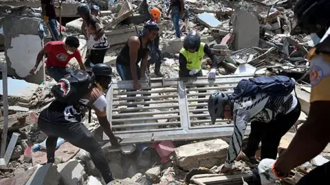 Getty Images Volunteers lift a metal gate as they search through debris on the rubble of collapsed buildings in Catia La Mar.