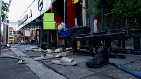 BBC/Lulu Luo Pairs of slightly charred slippers strewn on a street outside the bar, with high stools in the background.