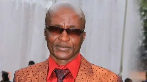 March and March Andile Mvuyelwa Somgxada in sunglasses wearing a red shirt maroon patterned tie and an orange and brown check tailored jacket