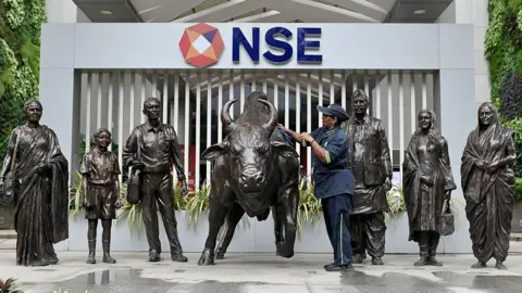 Bloomberg via Getty Images An employee cleans the metallic bull sculpture at the NSE headquarters. There are several other metallic sculptures of men and women around the bull. 