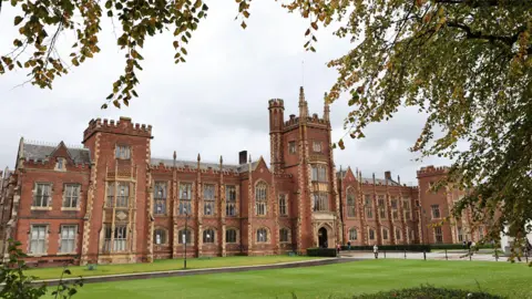 Why are so many organisations leaving X? PA Media A photo of Queen's University main building (the Lanyon building), it's red bricked with smaller yellow masonry around the windows, which consist of 3 floors of windows and larger windows on the top floor. A central tower is the main entrance with four floors of windows. The building sits on a patch of green grass with a walkway to the main entrance.