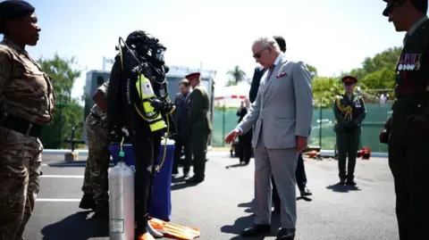 PA Media The King wearing a suit gestures towards equipment that is being demonstrated    by the Royal Bermuda Regiment Coast Guard