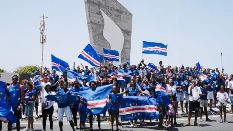 Thousands welcome home Cape Verde footballers after stunning World Cup run Michel Mvondo/BBC A group of fans, wearing the blue national kit, wave Cape Verde flags.