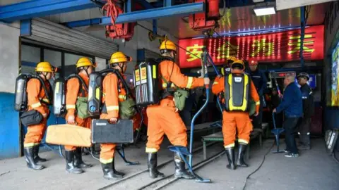 At least 82 killed in Chinese coal mine explosion Xinhua Rescue workers in orange gear entering industrial facility with equipment and breathing apparatus.