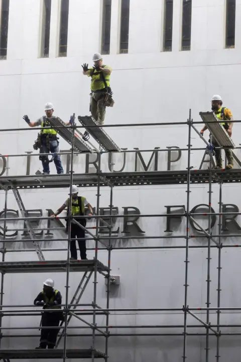 Reuters Workers stand on scaffolding in front of the sign and gesture