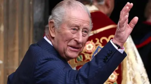 EPA/Shutterstock King Charles, dressed in a blue pinstriped suit, is smiling and waving at the entrance of St. George's Chapel, Windsor