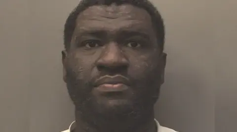 Merseyside Police A mug shot of Kwame Yeboah. He has short dark curly hair and is staring into the camera.