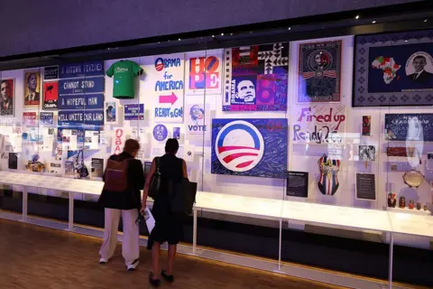 Talia Sprague/Bloomberg via Getty Images People stand and look at an exhibit of campaign merchandise and supporter-made memorabilia from Obama's presidential campaigns