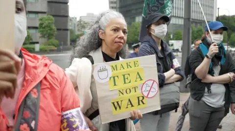 Anti-war protests rock Japan as PM pushes for stronger defence BBC News: Jiro Akiba A woman with grey hair holds a sign that says 'Make tea not war'