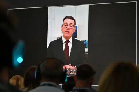 Getty Images A pre-recorded message by UK Prime Minister Andy Burnham is played prior a speech by Defence Secretary Wes Streeting during the Farnborough International Air Show 2026