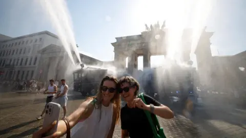 Reuters Two women take a selfie as they stand under mist fired from two police water cannons