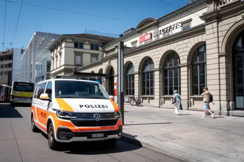 EPA A mid-shot of a white and orange Swiss police van parked outside Winterthur train station after a stabbing attack suspect was arrested.