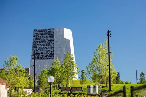 Universal Images Group via Getty Images The Obama Presidential Center, a large modern stone building, rises over a lush green park and benches in Chicago