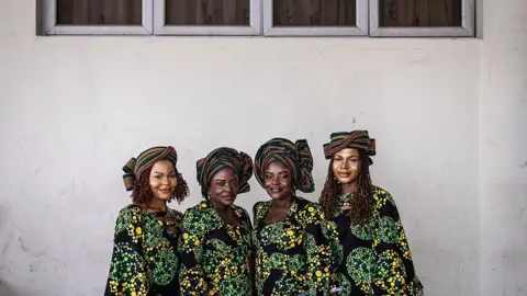 AFP via Getty Images  Twin sisters Taiwo and Kehinde Oketikun pose for a photograph with twin sisters Taiwo and Kehinde Adisa. All four wear matching multi-coloured outfits.