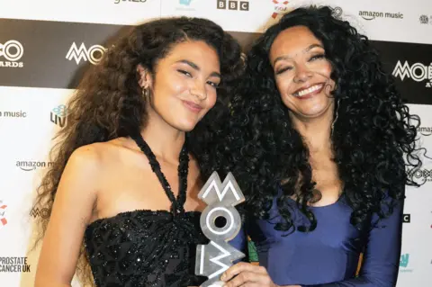 PA Media Olivia Dean and Kanya King standing together and smiling, holding a Mobo Award between them