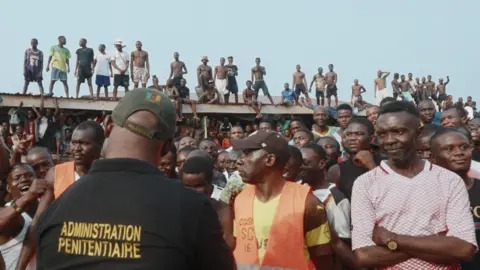 The notorious Cameroonian prison with its own record label Artists Equity Inmates form a crowd in the courtyard - some of them can be seen standing on a corrugated iron roof.